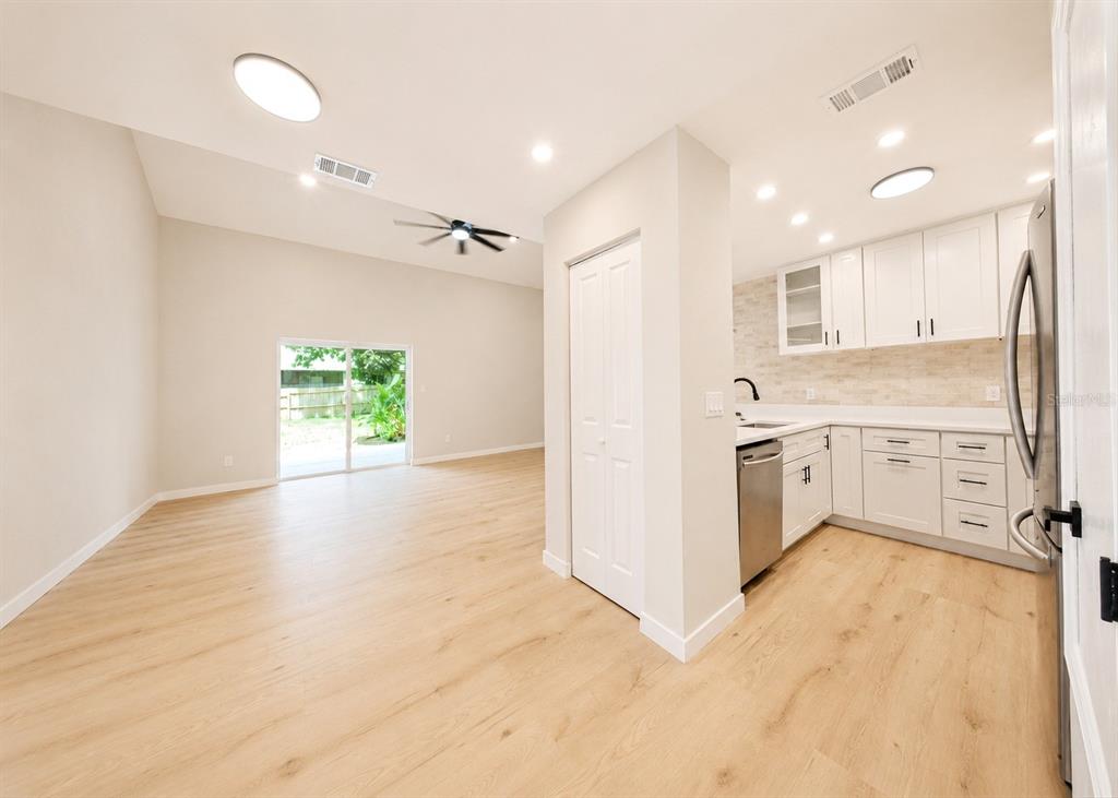 A kitchen with white cabinets and light wood flooring opens into a living area — 1141 WOODMAN WAY, ORLANDO, FL