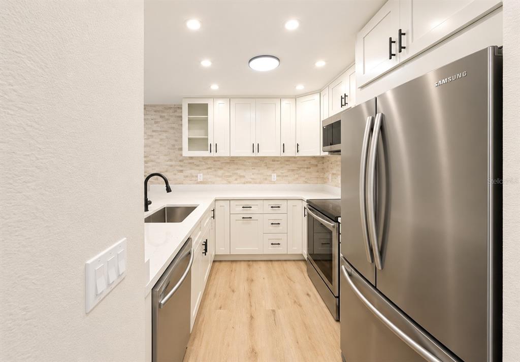 A modern kitchen features white cabinets, stainless steel appliances, and light wood-look flooring — 1141 WOODMAN WAY, ORLANDO, FL