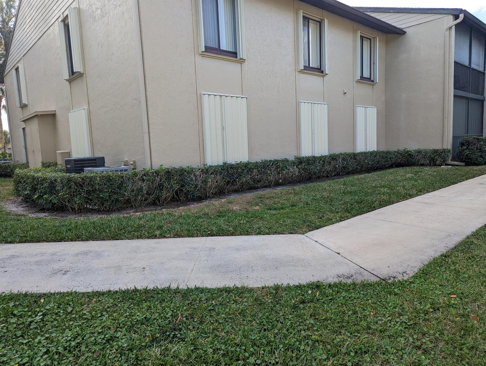 A beige multi-story apartment building exterior features a manicured hedge and a concrete walkway — 702 Sunny Pine Way # G1, FL 33415, FL