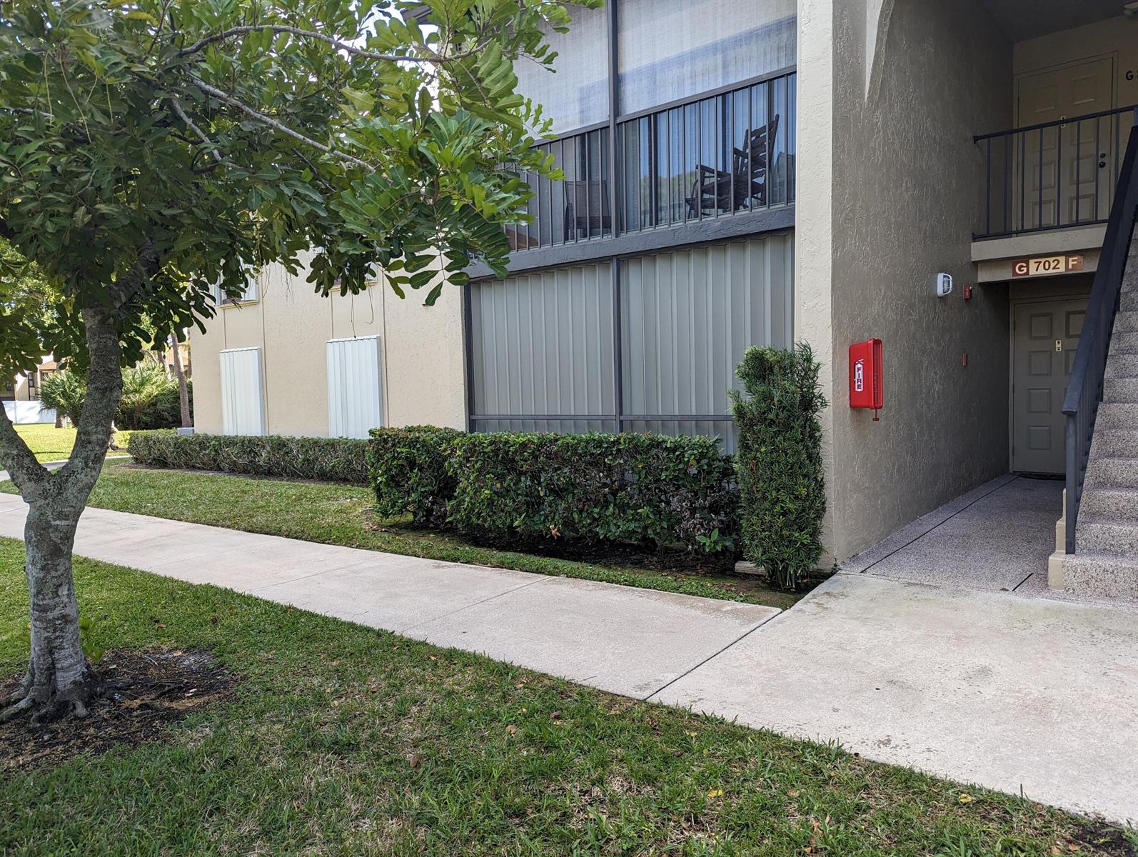 Exterior view of a multi-story apartment building with a sidewalk, landscaping, and a fire extinguisher — 702 Sunny Pine Way # G1, FL 33415, FL