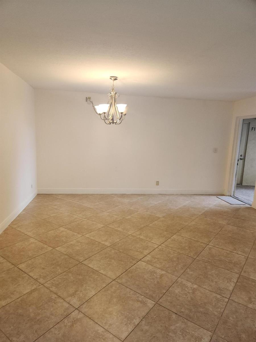 An empty room with beige tile flooring, white walls, and a hanging brass chandelier — 702 Sunny Pine Way # G1, FL 33415, FL