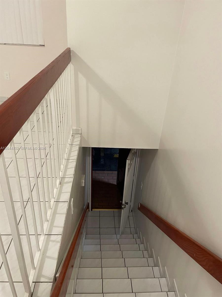 A staircase with white tile steps and wooden handrails leads down to a doorway — 10101 W Okeechobee Rd # 5202, Hialeah Gardens FL 33016, HIALEAH GARDENS, FL