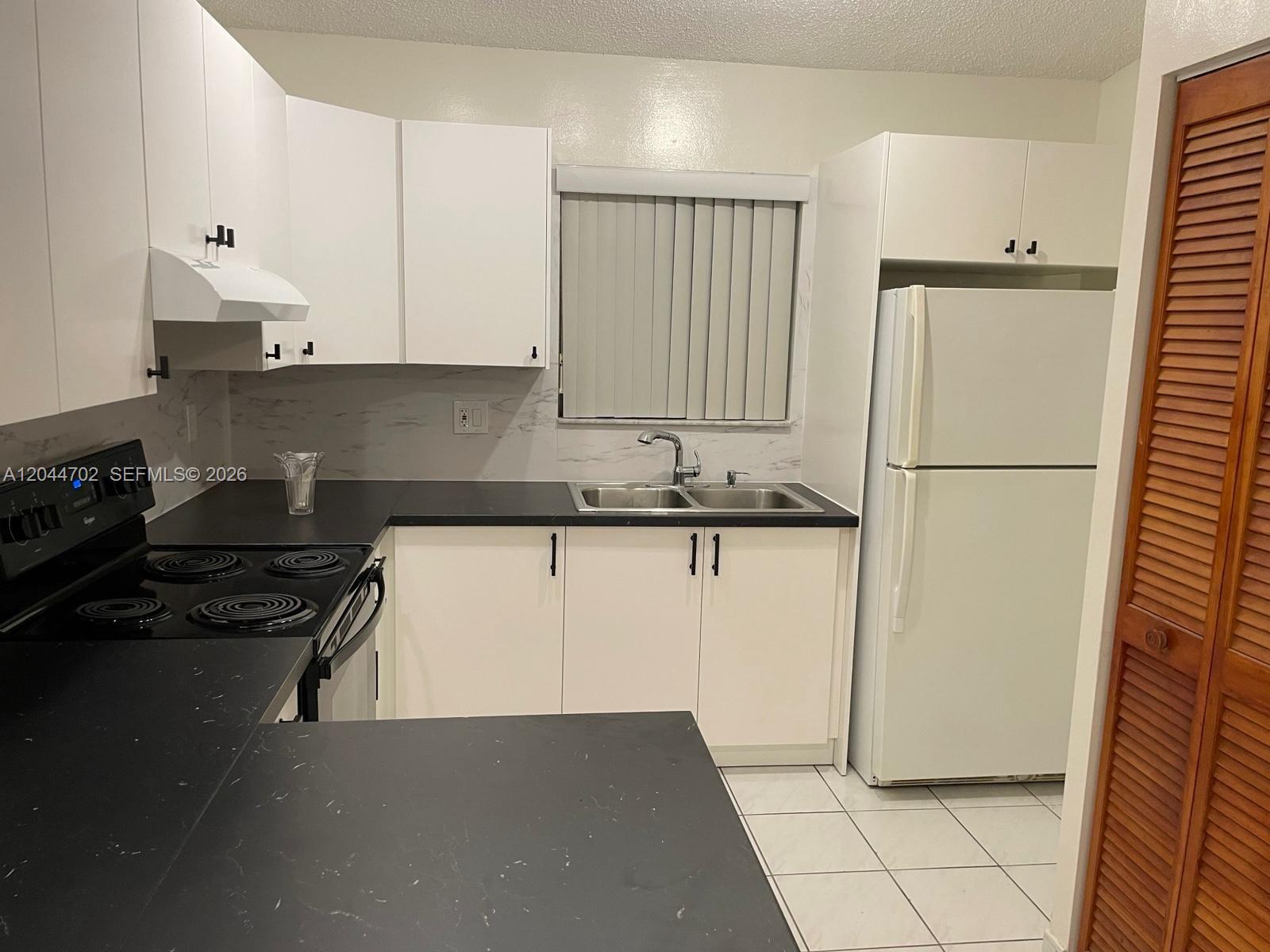 A kitchen features white cabinets, black countertops, a double sink, and white appliances — 10101 W Okeechobee Rd # 5202, Hialeah Gardens FL 33016, HIALEAH GARDENS, FL