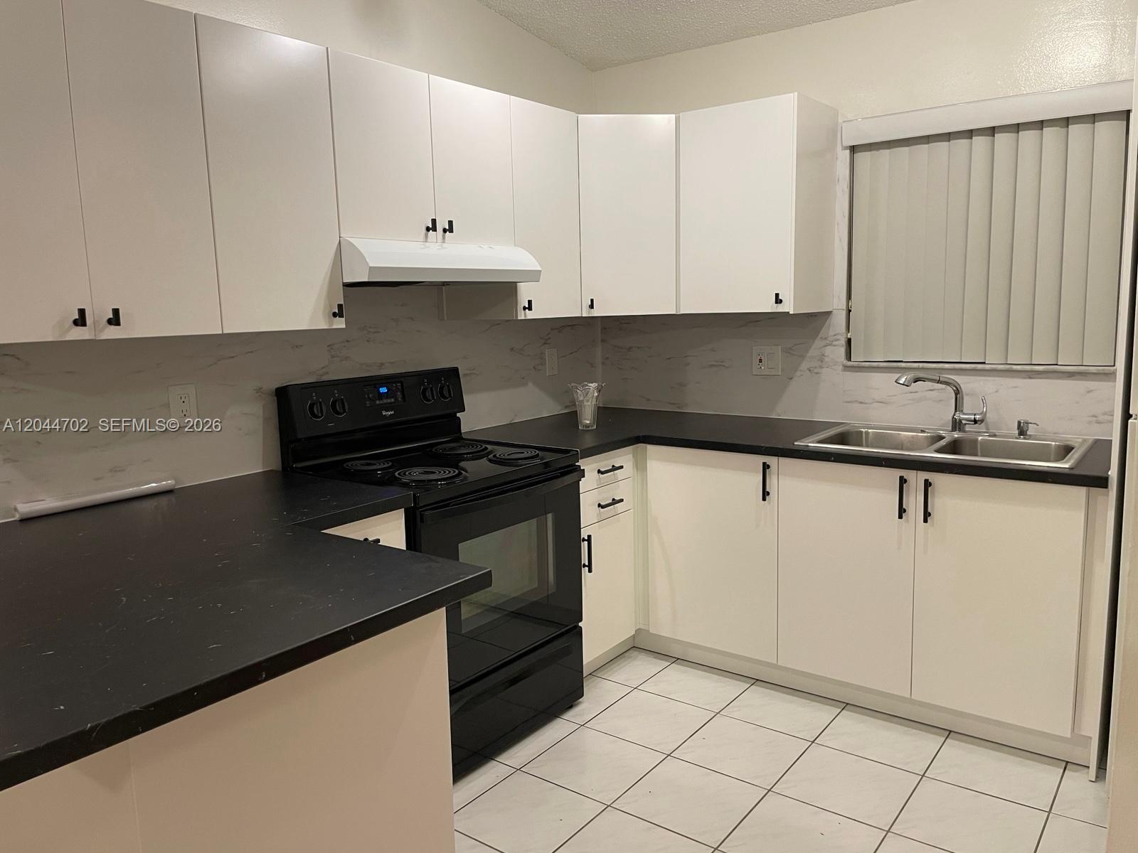 A kitchen features white cabinets, black countertops, a black stove, and a marble-patterned backsplash — 10101 W Okeechobee Rd # 5202, Hialeah Gardens FL 33016, HIALEAH GARDENS, FL
