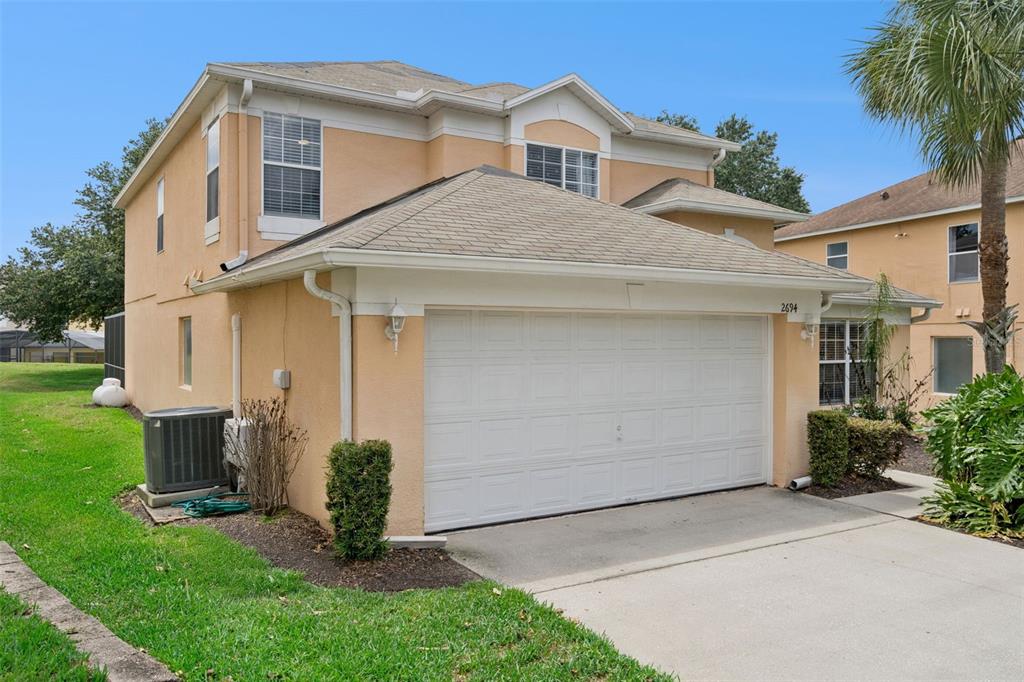 A two-story tan stucco house with a white two-car garage and a concrete driveway — 2694 LA ISLA COURT, KISSIMMEE, FL