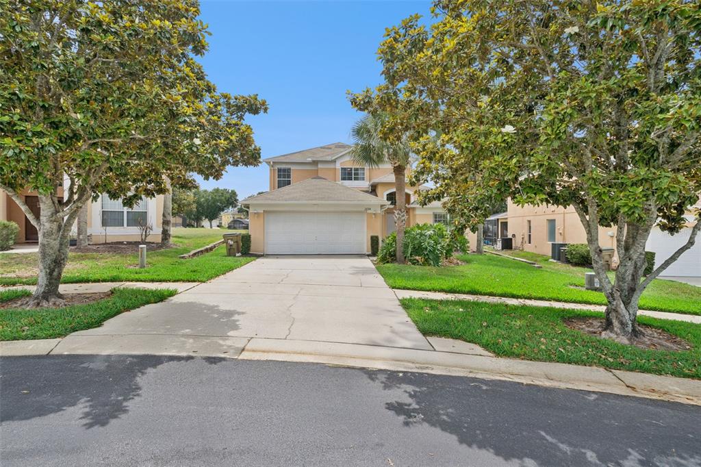 A two-story suburban house with a concrete driveway, a two-car garage, and mature trees — 2694 LA ISLA COURT, KISSIMMEE, FL