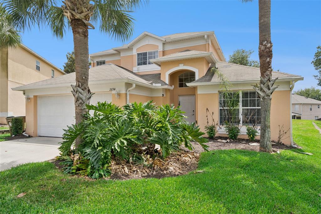 A two-story, peach-colored suburban house features a two-car garage and a large front garden — 2694 LA ISLA COURT, KISSIMMEE, FL