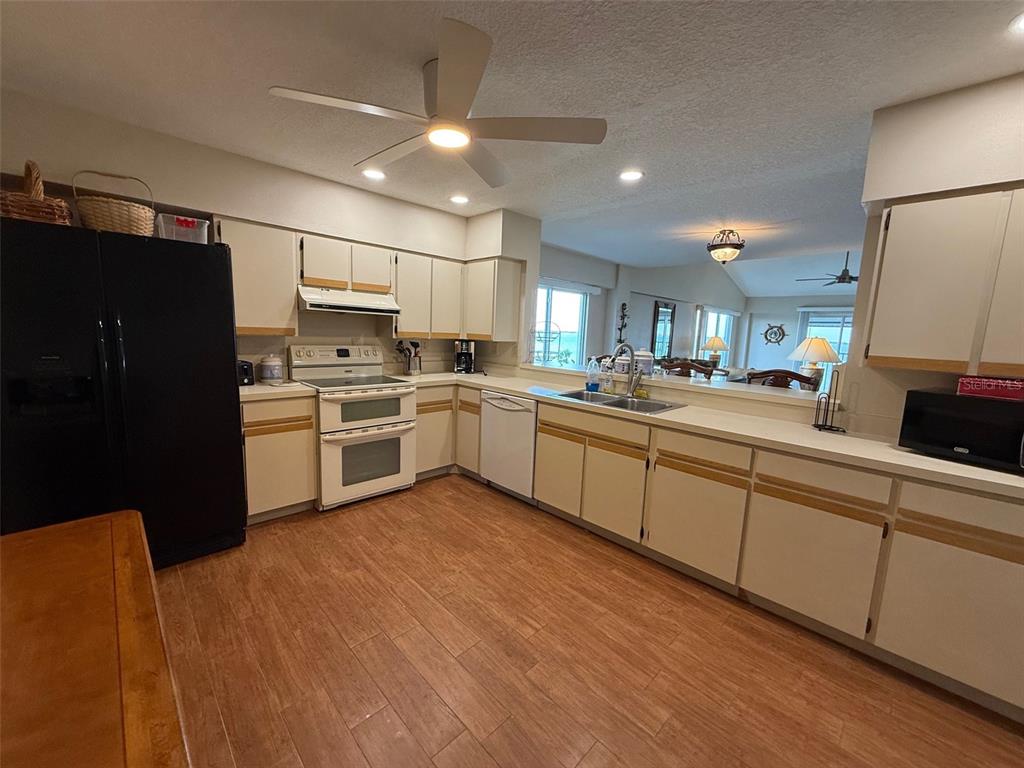 A kitchen with white cabinets, black refrigerator, light wood-look flooring, and a breakfast bar — 1477 PARK BEACH CIRCLE UNIT 31, PUNTA GORDA, FL