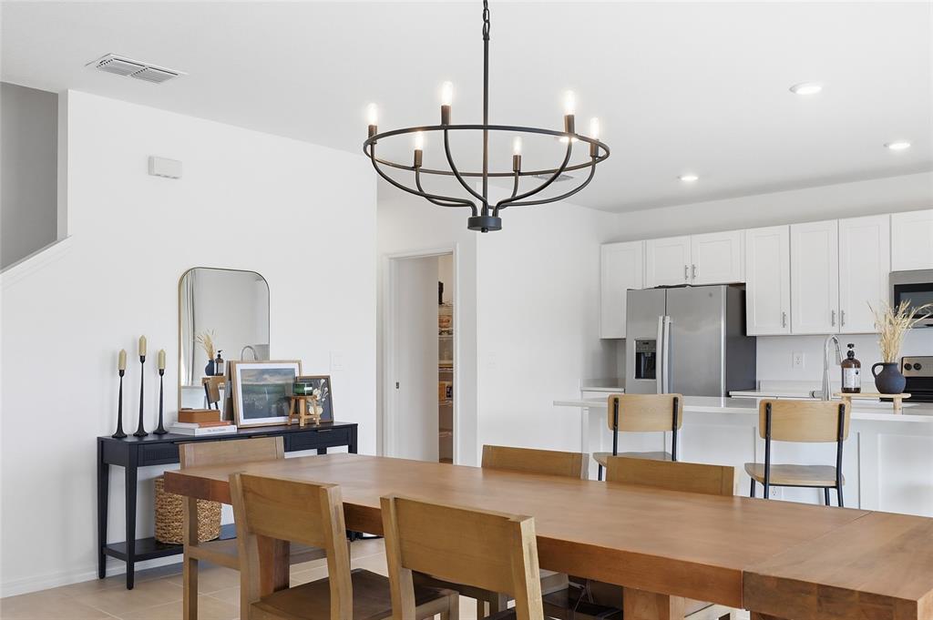 A dining area with a wooden table and chandelier opens into a modern white kitchen — 1017 CALICO POINTE CIRCLE, GROVELAND, FL