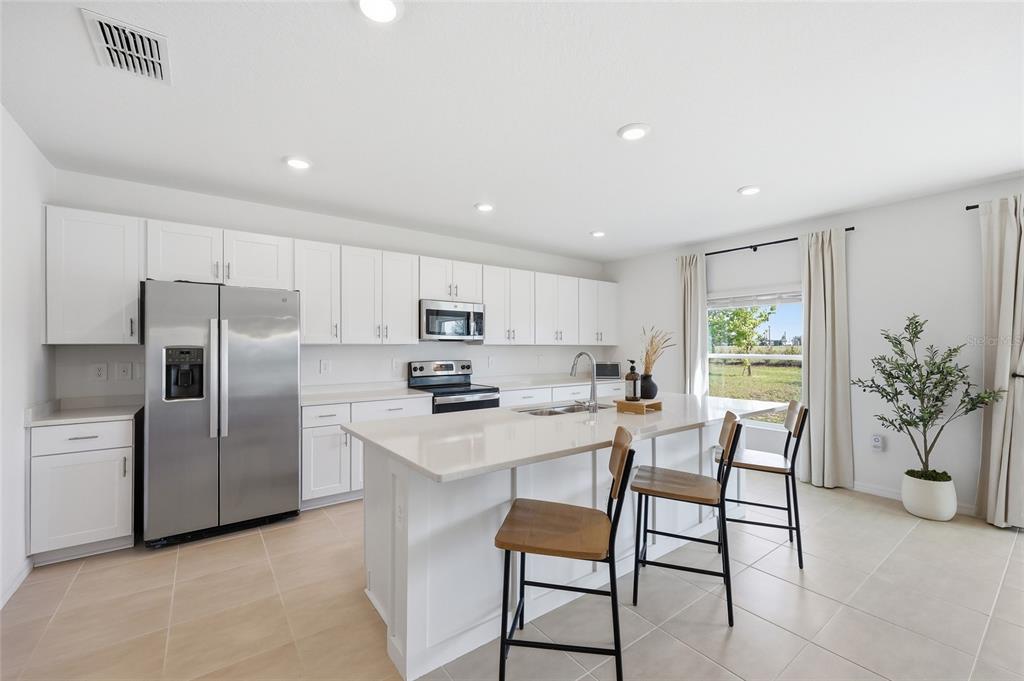 A modern kitchen features white cabinets, stainless steel appliances, a quartz island, and tile flooring — 1017 CALICO POINTE CIRCLE, GROVELAND, FL
