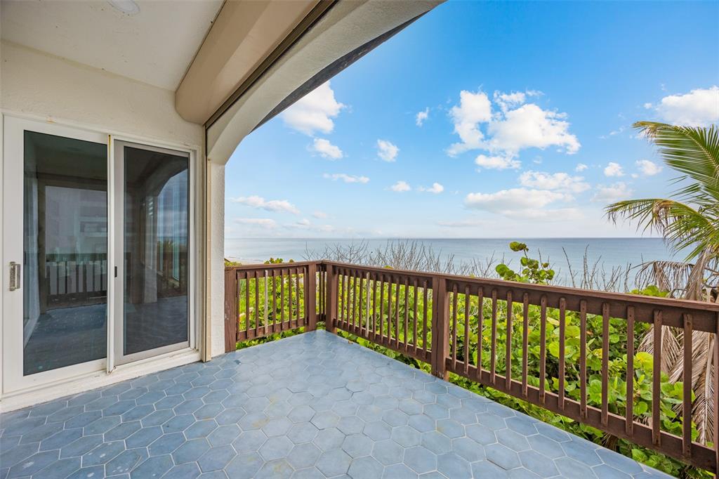 A balcony with blue hexagonal tile flooring and a wooden railing overlooking the ocean — 5595 S HIGHWAY A1A, MELBOURNE BEACH, FL