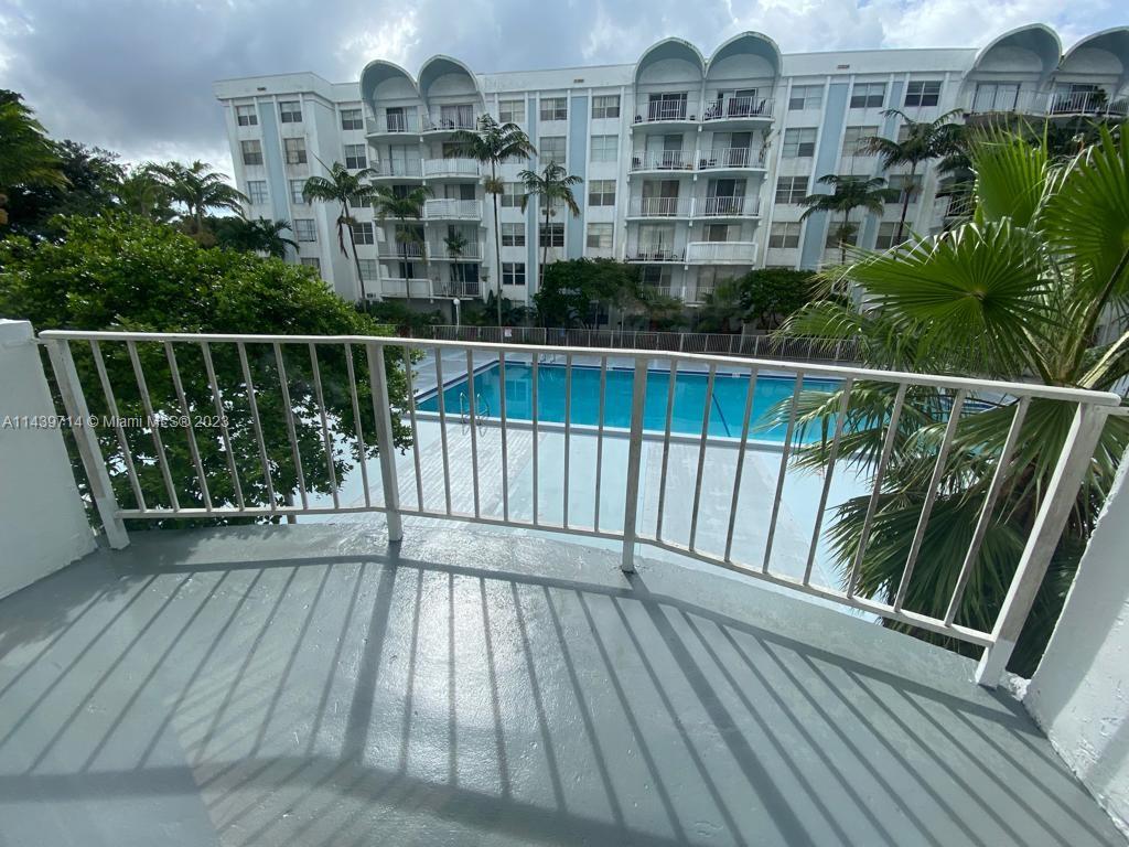 A balcony with a white railing overlooks a swimming pool and a multi-story apartment building — 498 NW 165th St Rd # D401, Miami FL 33169, MIAMI, FL