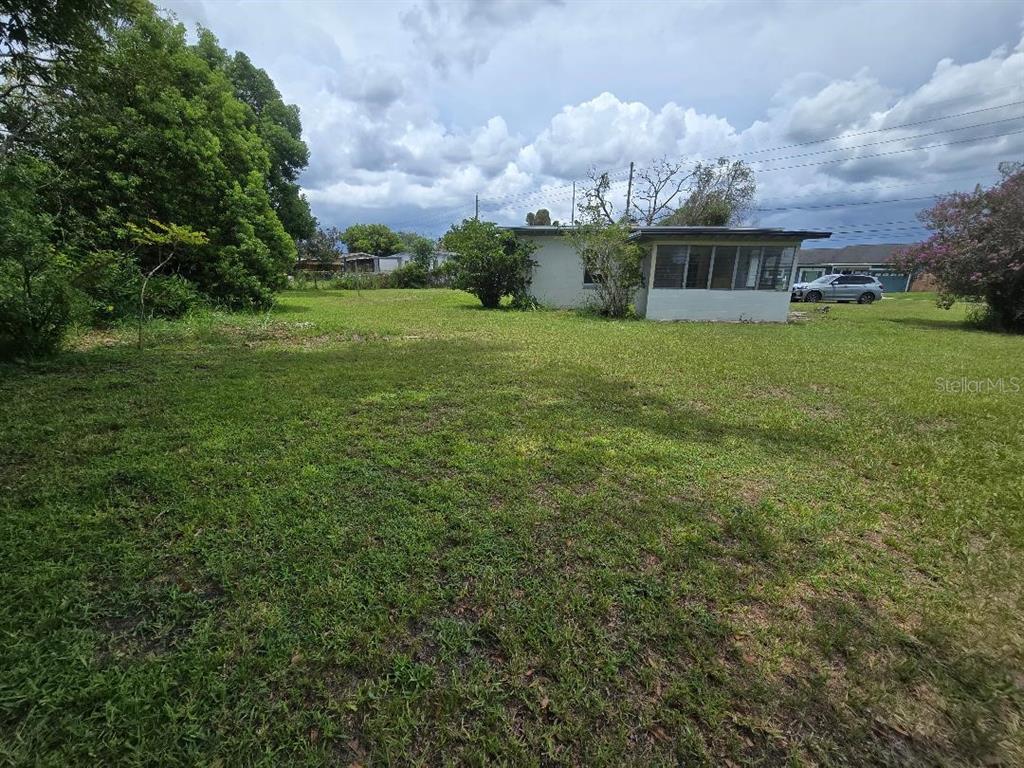 A grassy backyard leads to a small, single-story house with a screened-in porch — 5762 DOGWOOD DRIVE, ORLANDO, FL
