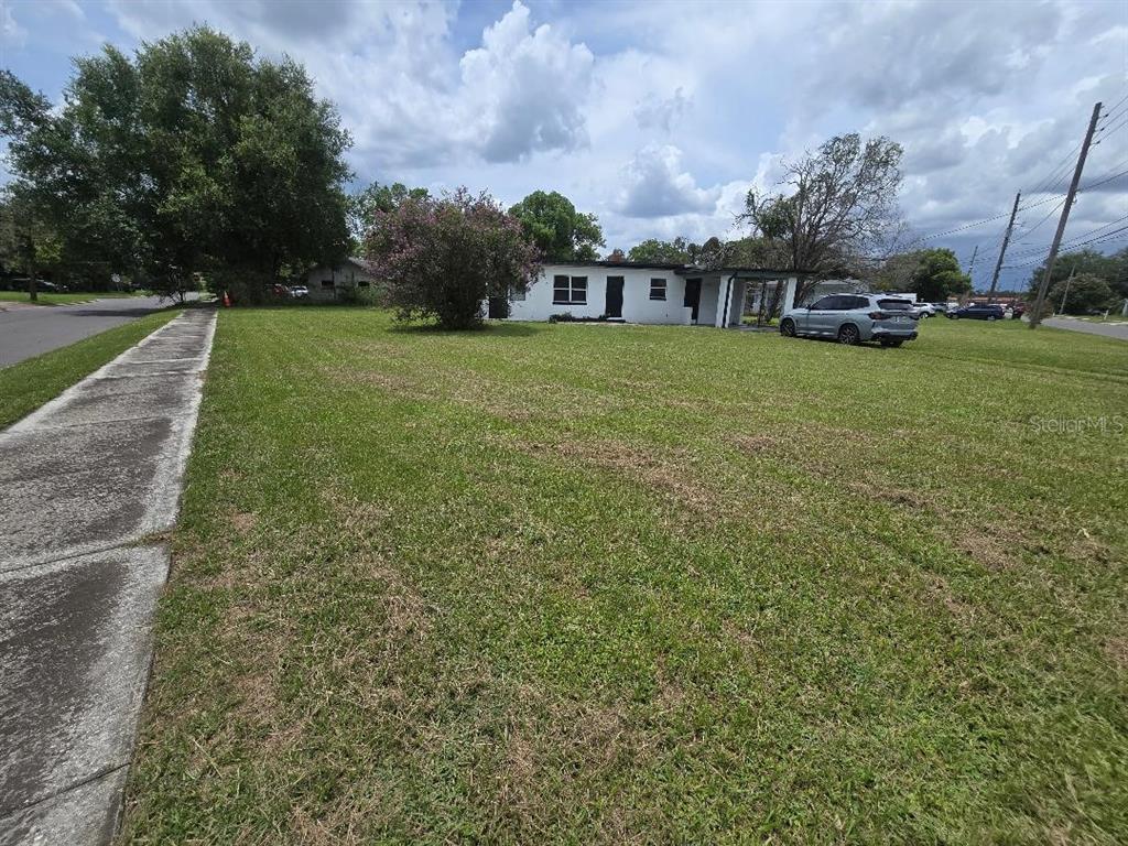 A single-story white house sits on a large grassy lot next to a sidewalk — 5762 DOGWOOD DRIVE, ORLANDO, FL
