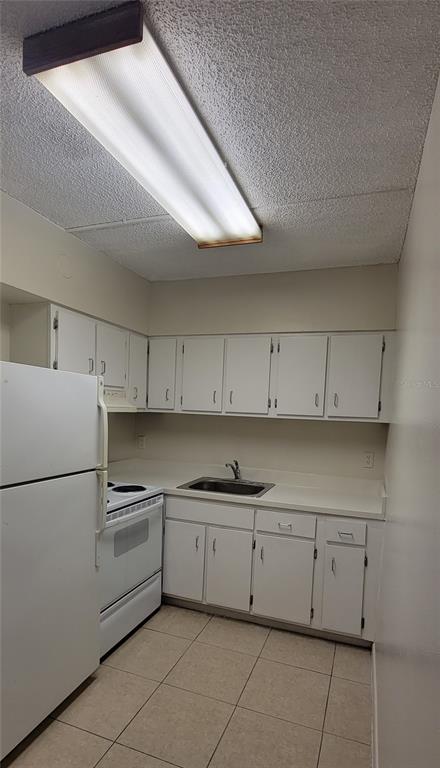 A galley kitchen features white cabinets, white appliances, a stainless steel sink, and tiled flooring — 3810 W SAN CARLOS STREET UNIT 314, TAMPA, FL