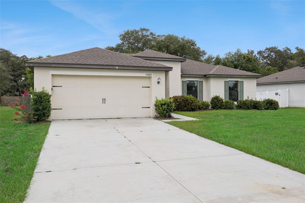 A single-story house with a beige stucco exterior, a two-car garage, and a concrete driveway — 35685 ROSE MOSS AVENUE, LEESBURG, FL