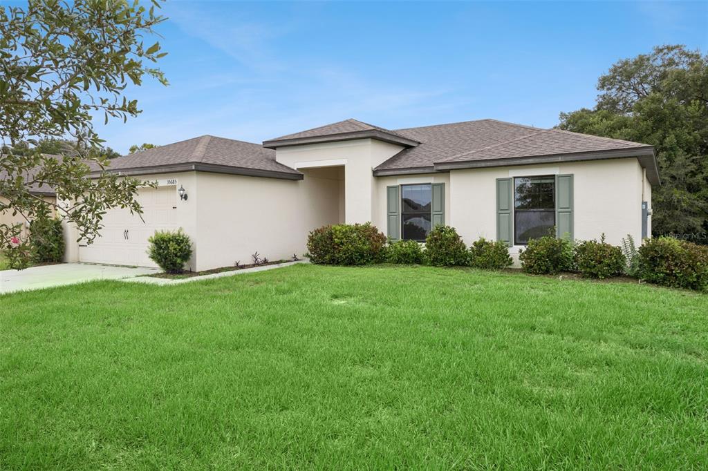 A single-story house with a beige stucco exterior, a two-car garage, and green shutters — 35685 ROSE MOSS AVENUE, LEESBURG, FL