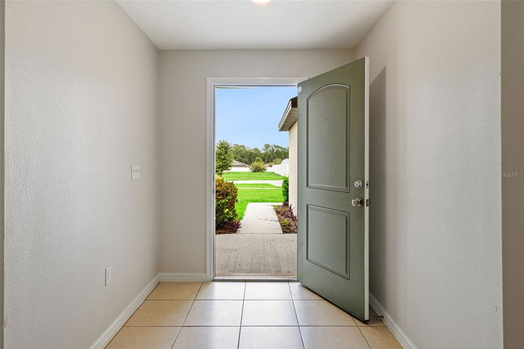 An entryway with beige tile flooring and an open door leading to a grassy yard — 35685 ROSE MOSS AVENUE, LEESBURG, FL