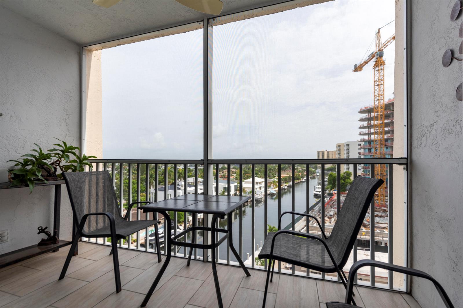A screened-in balcony features a small table, two chairs, and a view of a canal — 1391 S Ocean Boulevard # 801, Pompano Beach FL 33062, POMPANO BEACH, FL