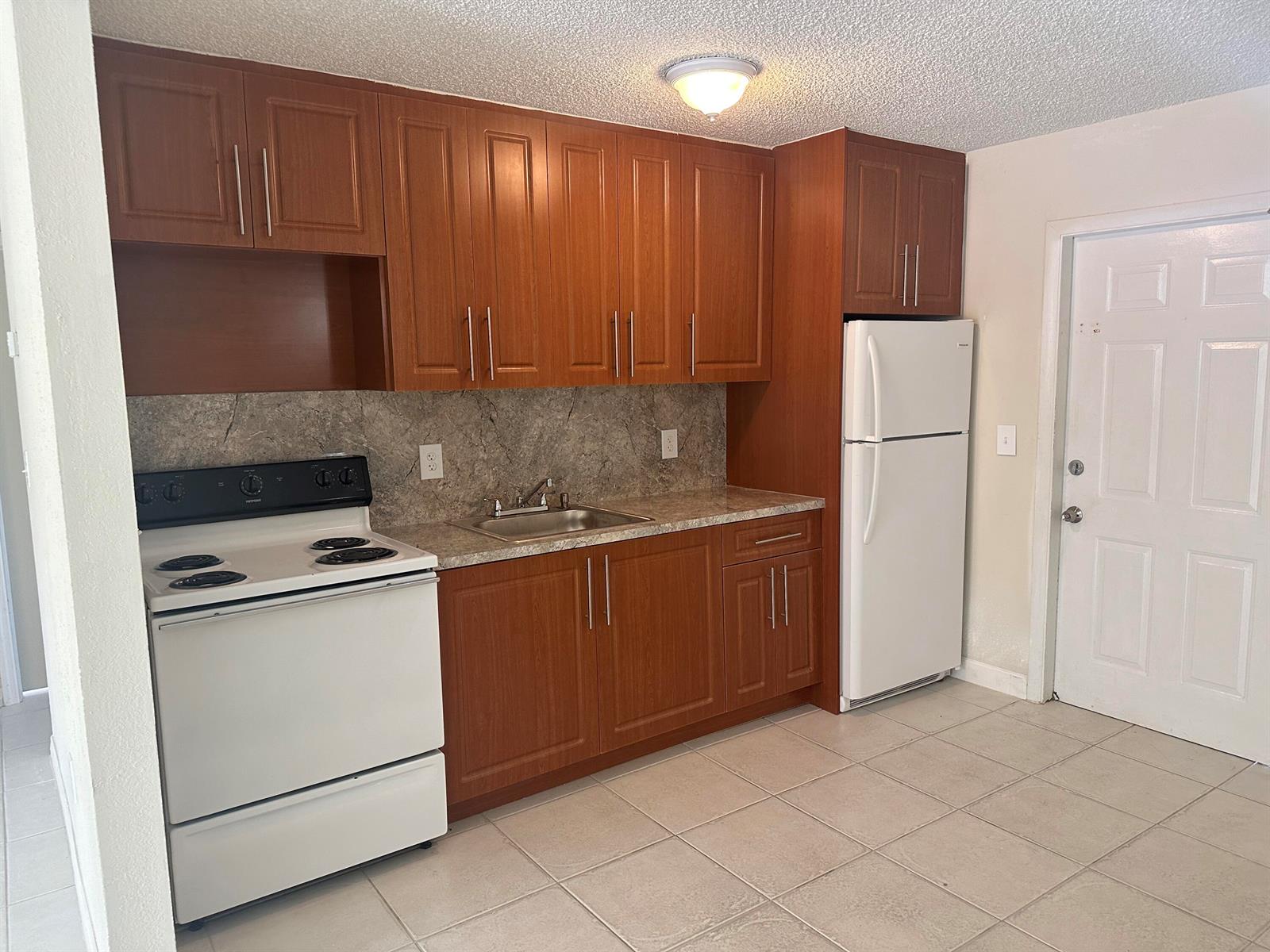 A kitchen features wood cabinets, white appliances, a stone-look backsplash, and light tile flooring — 422 Caroline Avenue, FL 33413, FL