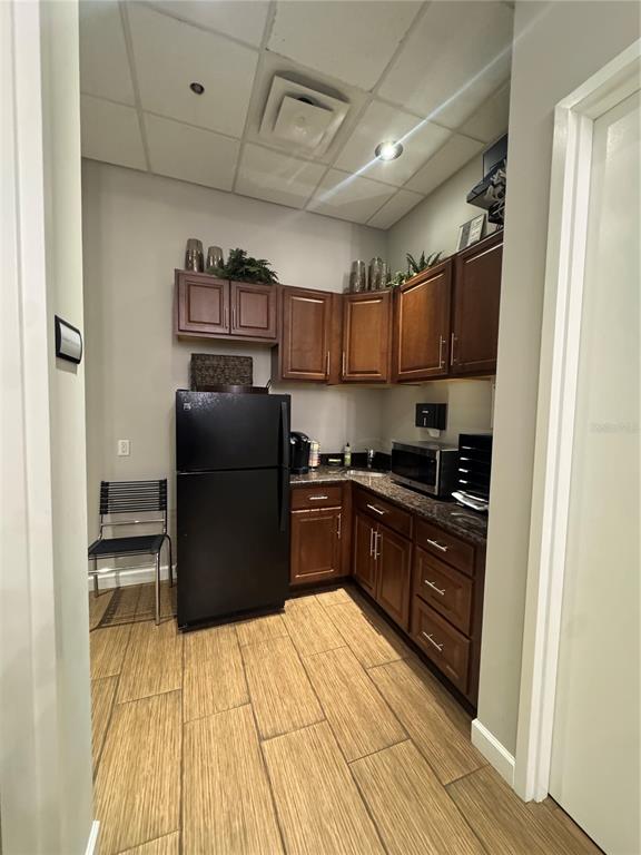 A small kitchen features dark wood cabinets, a black refrigerator, and wood-look tile flooring — 1112 CHANNELSIDE DRIVE UNIT CU3, TAMPA, FL
