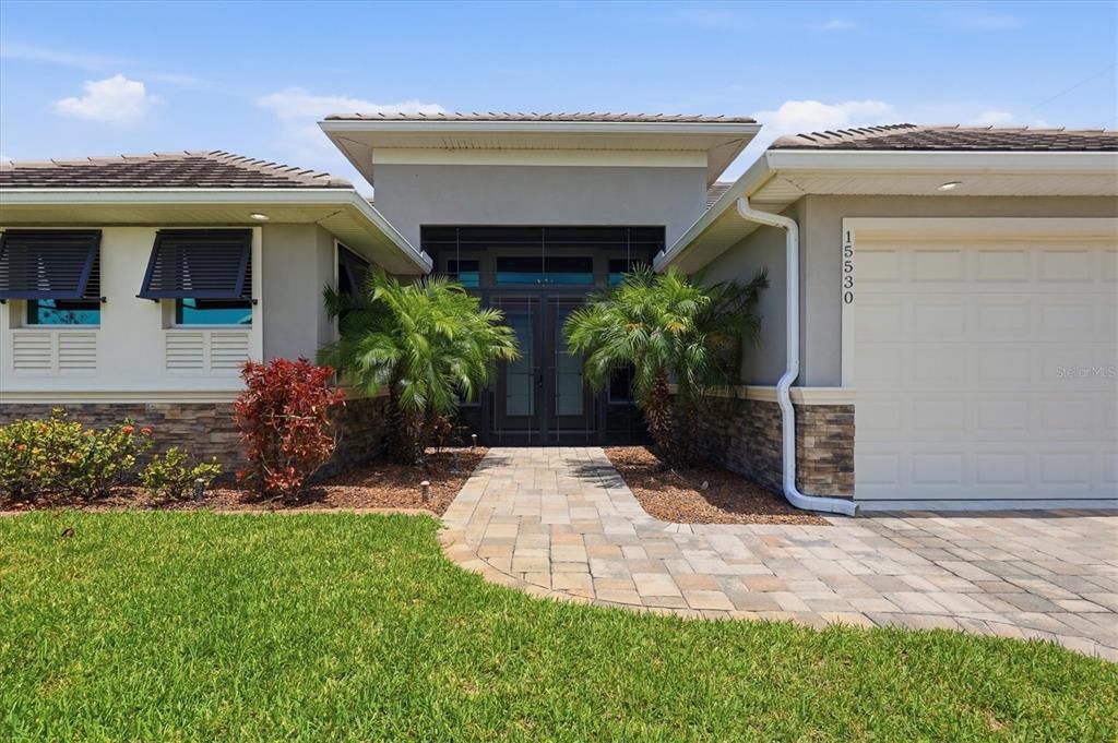 The front exterior of a single-story house features a stone facade, palm trees, and walkway — 15530 STAUNTON CIRCLE, PORT CHARLOTTE, FL