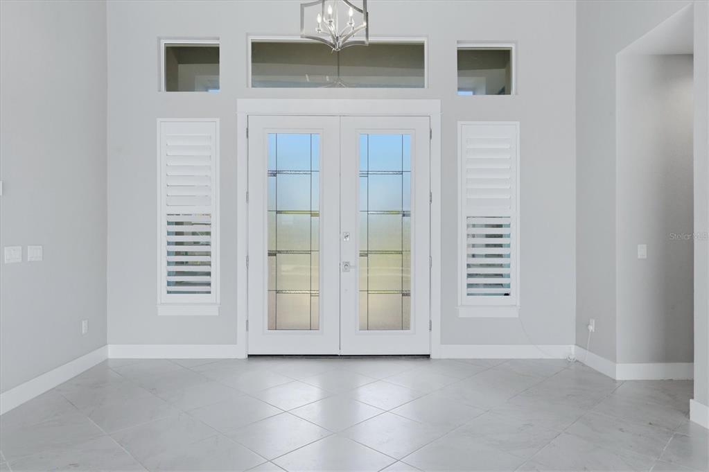 A bright entryway features double glass doors, white plantation shutters, and light-colored tile flooring — 15530 STAUNTON CIRCLE, PORT CHARLOTTE, FL