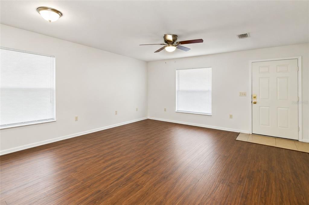 An empty living room features wood-look flooring, white walls, a ceiling fan, and a front door — 702 E MADISON STREET, PLANT CITY, FL