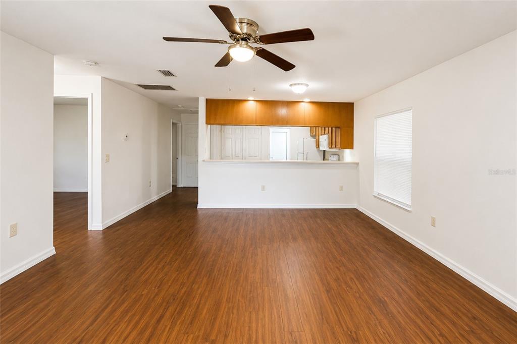 An empty living room with wood-look flooring, a ceiling fan, and a kitchen pass-through window — 702 E MADISON STREET, PLANT CITY, FL