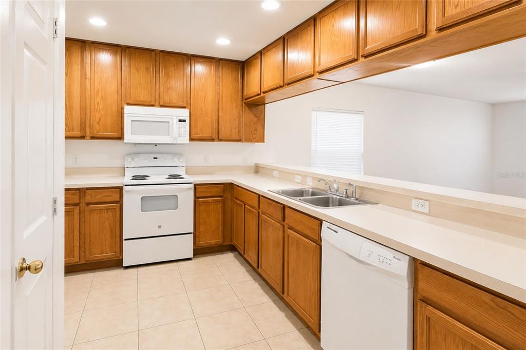A kitchen with wood cabinets, white appliances, tile flooring, and a breakfast bar counter — 702 E MADISON STREET, PLANT CITY, FL