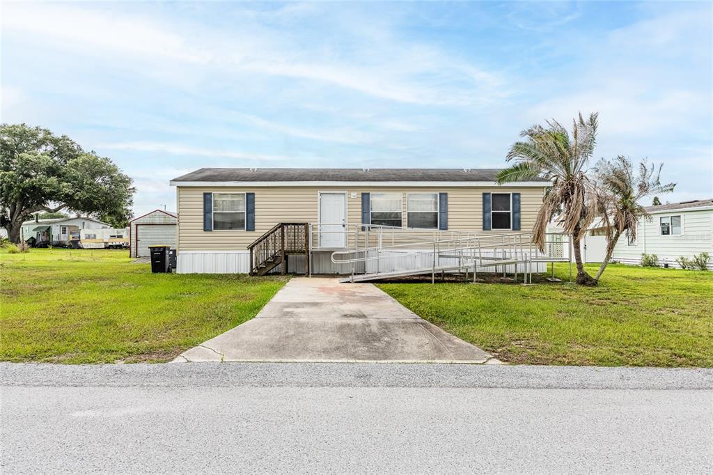 A single-story manufactured home with a concrete driveway, a wooden staircase, and a metal ramp — 2308 KAY STREET, LAKE ALFRED, FL