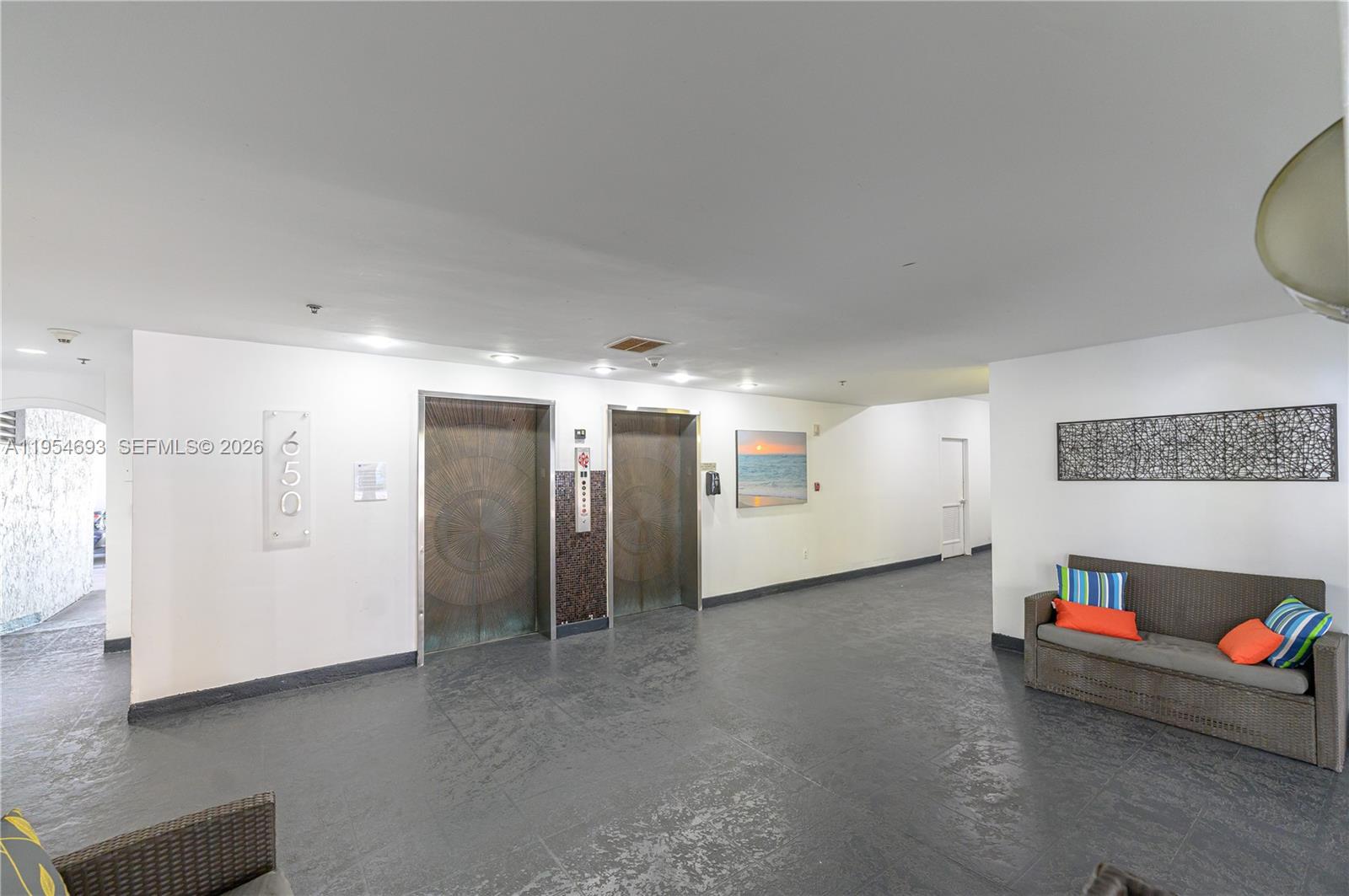 A lobby area features two elevators, a gray tiled floor, and a wicker sofa — 650 NE 64th St # G510, Miami FL 33138, MIAMI, FL