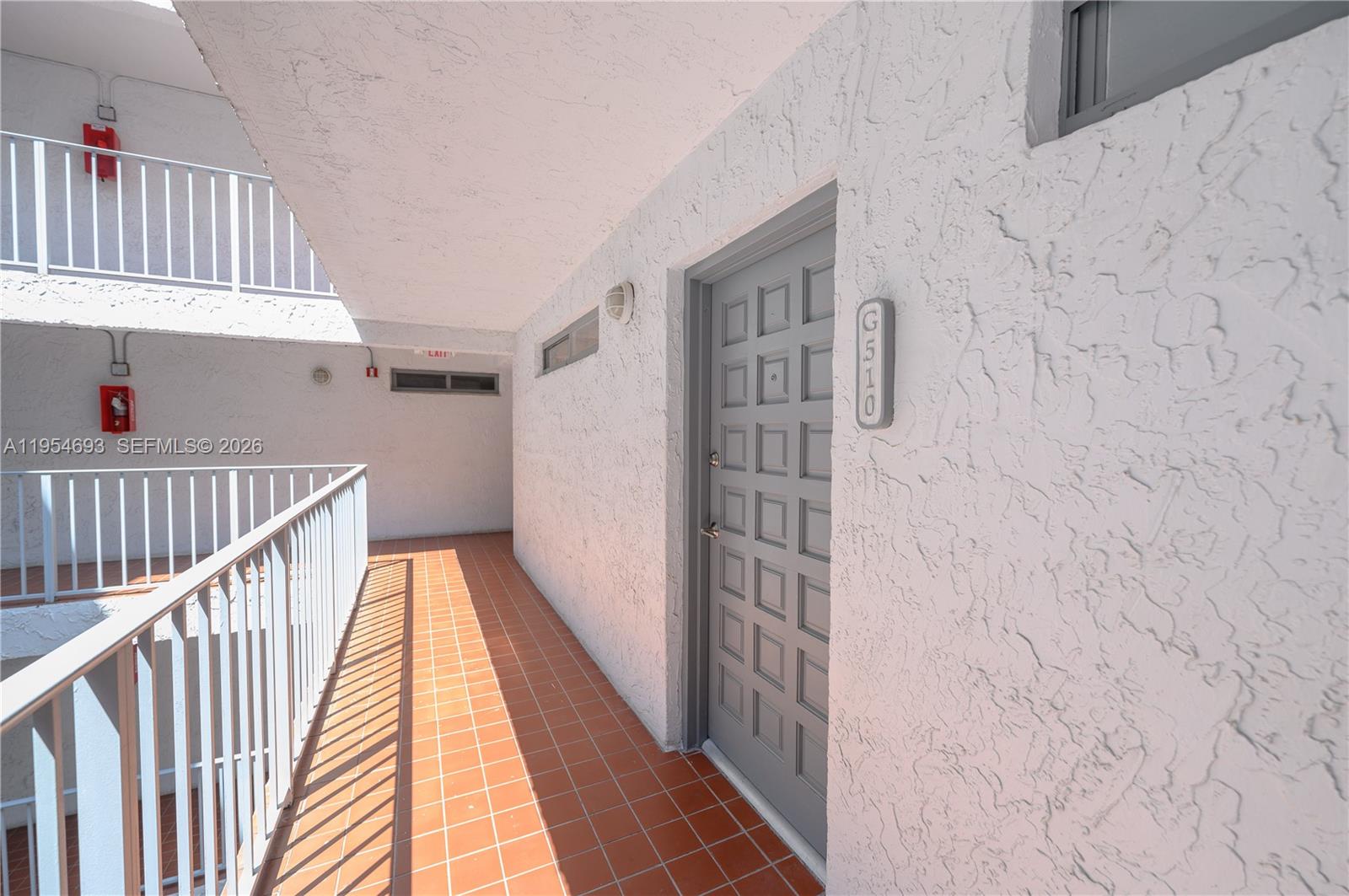 An outdoor walkway with orange tile flooring leads to a gray door labeled 6510 — 650 NE 64th St # G510, Miami FL 33138, MIAMI, FL