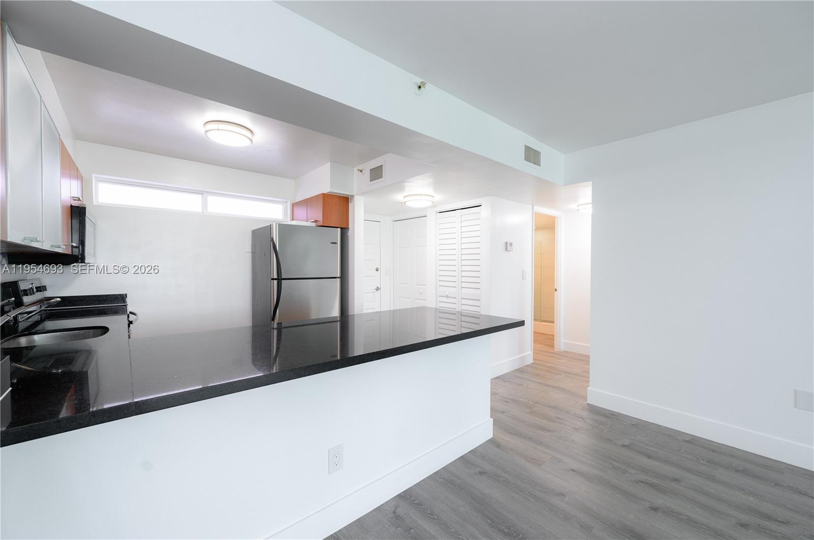 A kitchen features a black granite breakfast bar, stainless steel refrigerator, and wood-look flooring — 650 NE 64th St # G510, Miami FL 33138, MIAMI, FL