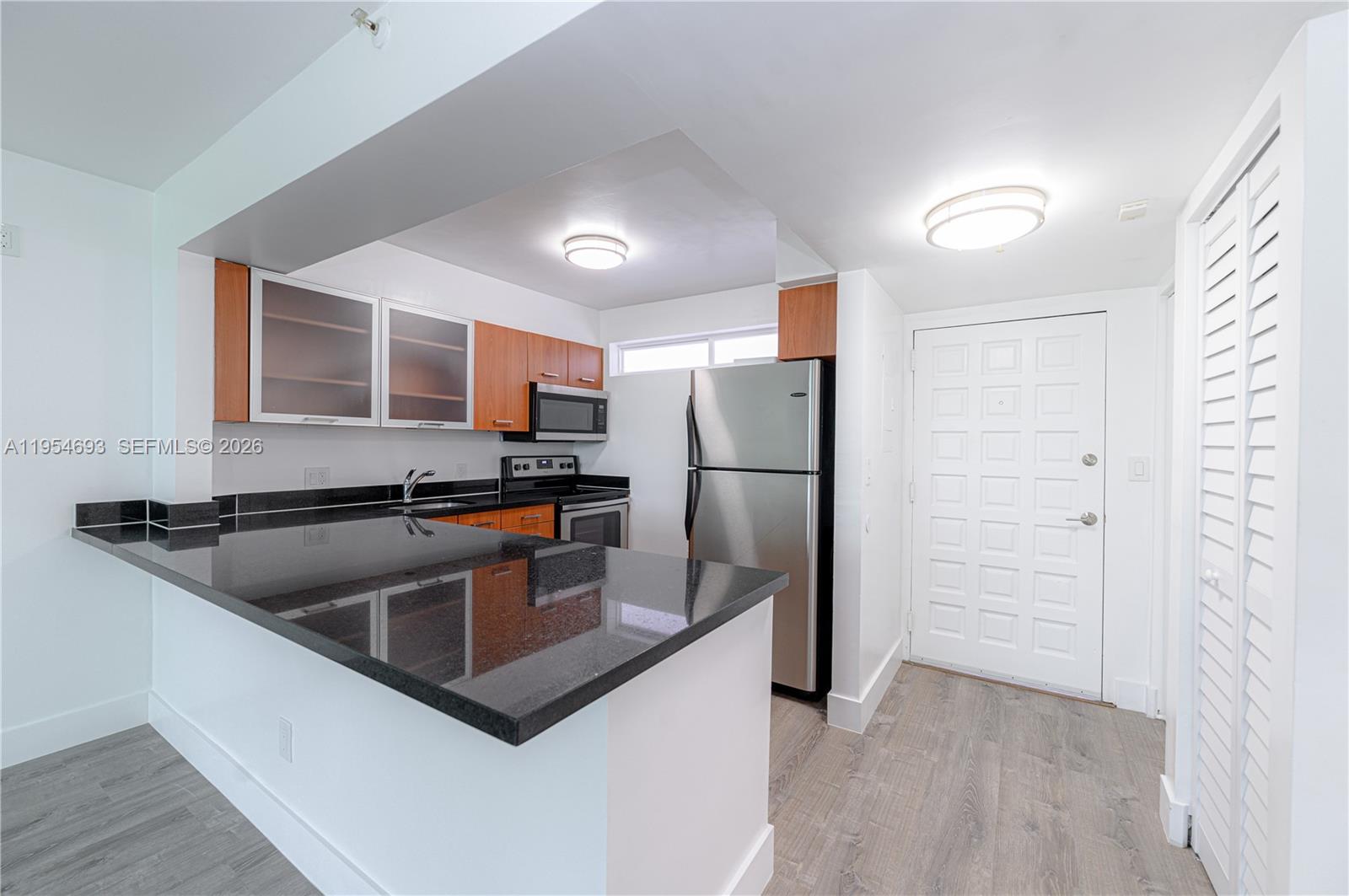 A kitchen features black countertops, wood-toned cabinetry, stainless steel appliances, and light-colored wood flooring — 650 NE 64th St # G510, Miami FL 33138, MIAMI, FL