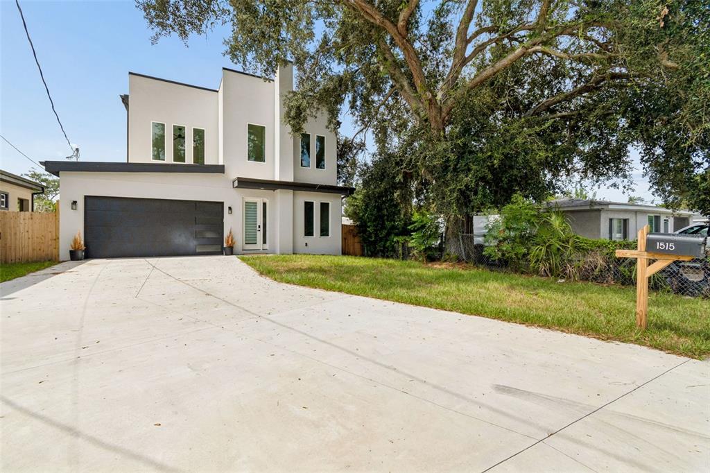A modern two-story house with a concrete driveway, a dark garage door, and large trees — 1515 E 27TH AVENUE, TAMPA, FL