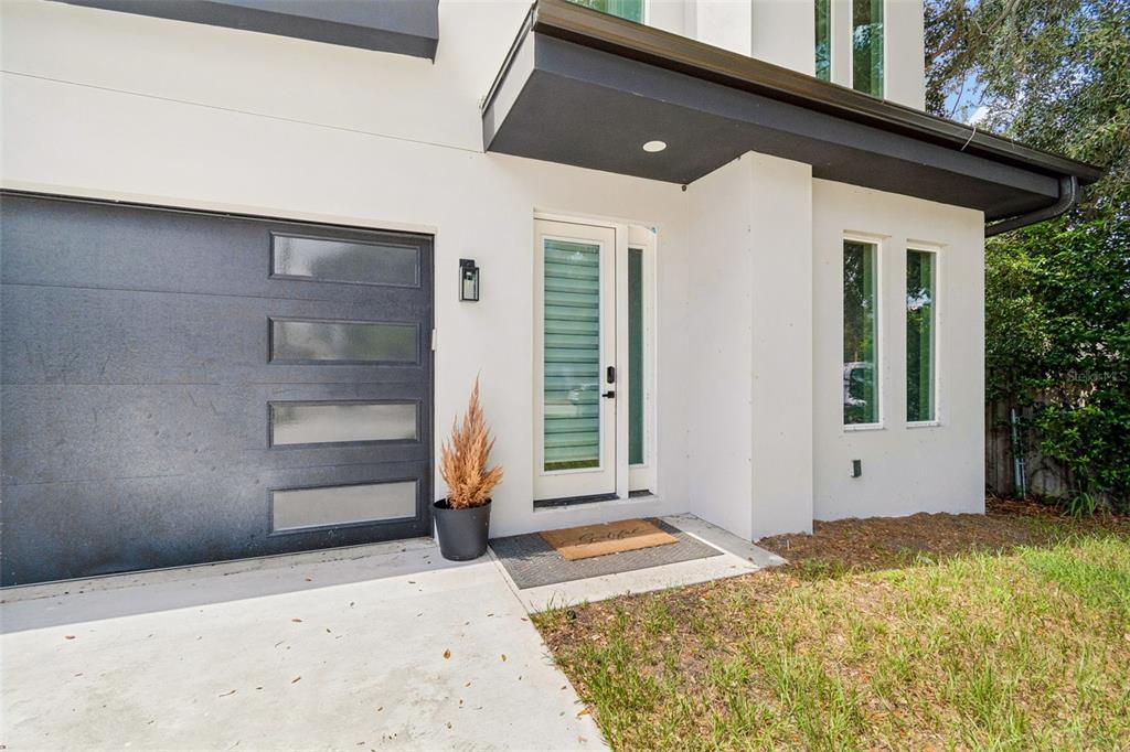 A modern home exterior features a dark garage door, a glass-paneled front door, and white stucco — 1515 E 27TH AVENUE, TAMPA, FL