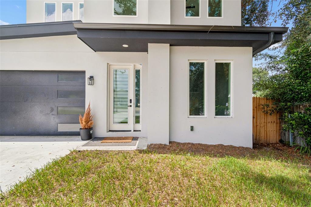 A modern two-story house exterior features a gray garage door, white stucco walls, and a glass-paneled door — 1515 E 27TH AVENUE, TAMPA, FL