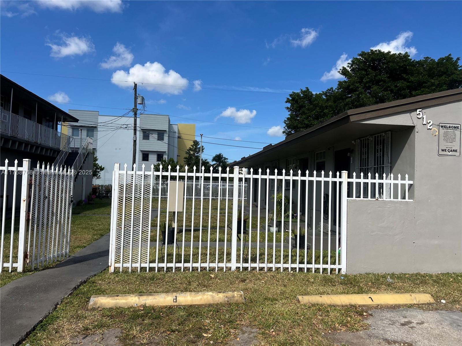 A white metal fence encloses a grassy yard in front of a single-story apartment building — 5100 NW 23rd Ave # 5, Miami FL 33142, MIAMI, FL
