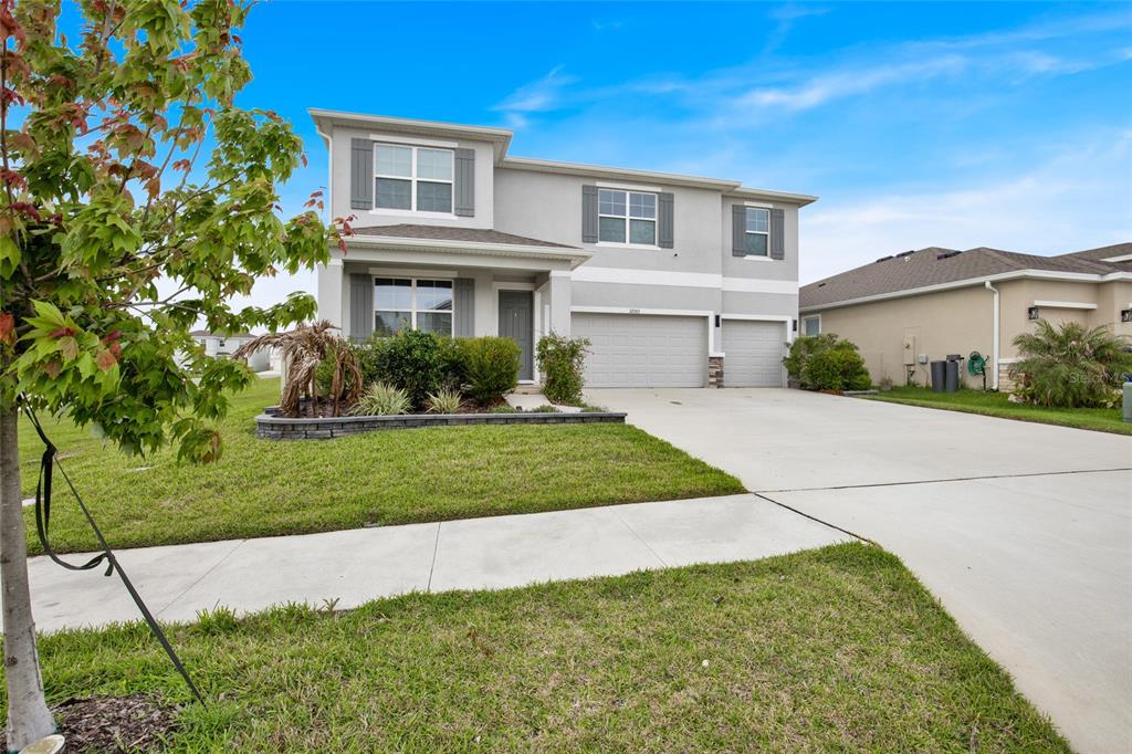 A two-story suburban house features a gray stucco exterior, a three-car garage, and landscaping — 32265 CONCHSHELL SAIL STREET, WESLEY CHAPEL, FL