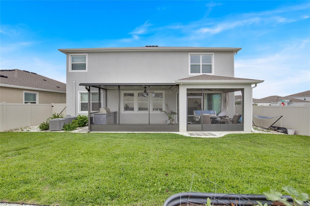The rear exterior of a two-story house features a screened-in patio and a fenced yard — 32265 CONCHSHELL SAIL STREET, WESLEY CHAPEL, FL