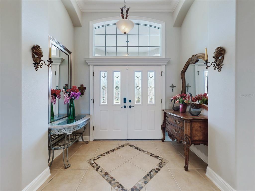 A bright entryway features double doors, a transom window, tile flooring, and two console tables — 649 TERNBERRY FOREST DRIVE, THE VILLAGES, FL