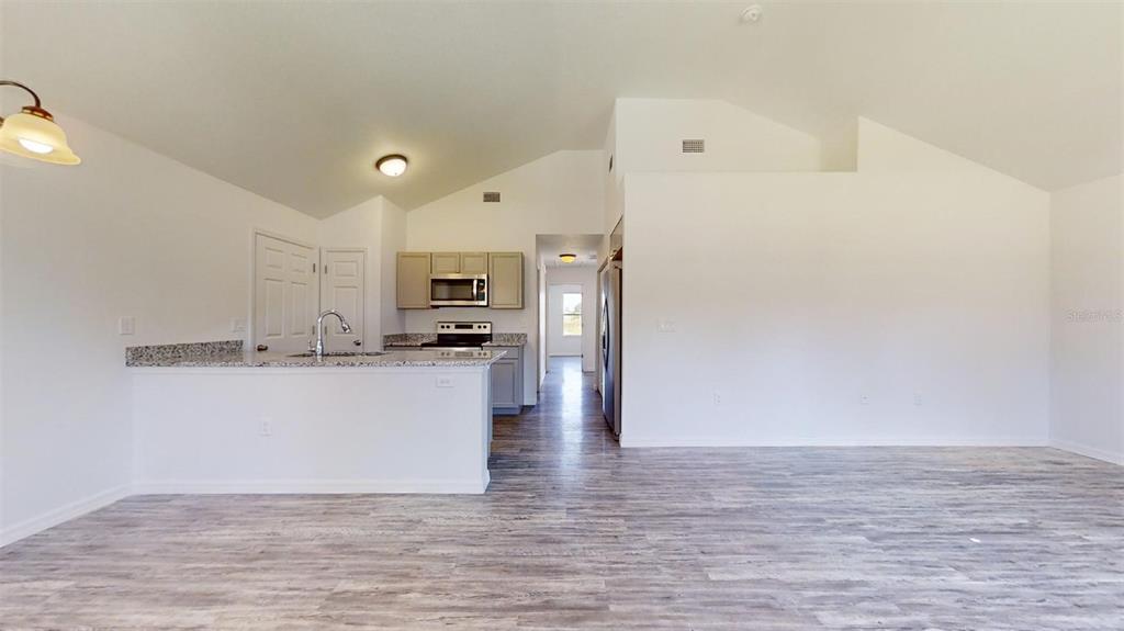 A kitchen with granite countertops and light wood cabinets overlooks a spacious, open-concept living area — 13739 SW 111TH LANE, DUNNELLON, FL