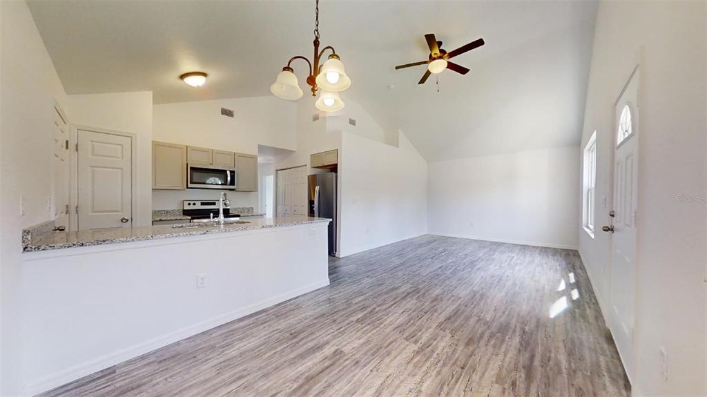 An open-concept kitchen and living area features light wood-look flooring and vaulted ceilings — 13739 SW 111TH LANE, DUNNELLON, FL