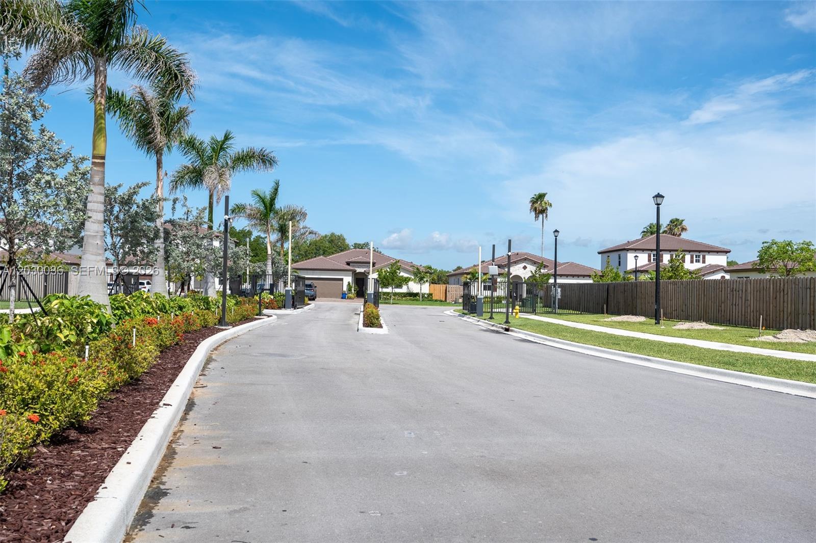 A paved driveway leads to a gated residential entrance lined with palm trees and landscaping — 2485 SE 29th Dr, Homestead FL 33035, HOMESTEAD, FL