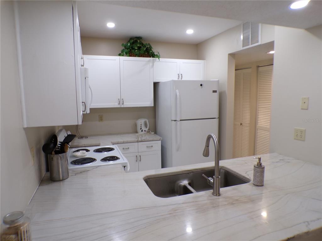 A kitchen features white cabinets, a white refrigerator, a stove, and a marble-patterned countertop — 622 BIRD BAY DRIVE S UNIT 203, VENICE, FL