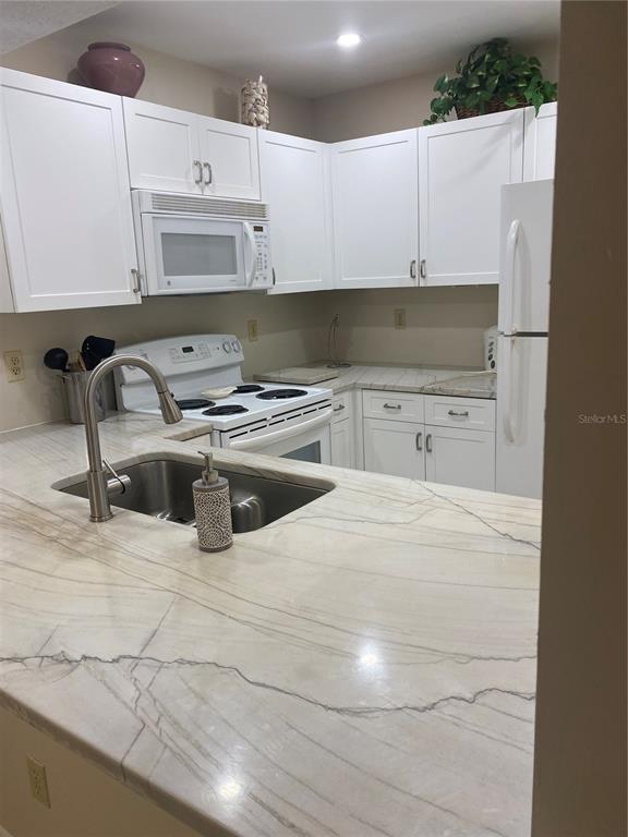 A kitchen features white cabinets, a white stove, and light-colored stone countertops with veining — 622 BIRD BAY DRIVE S UNIT 203, VENICE, FL
