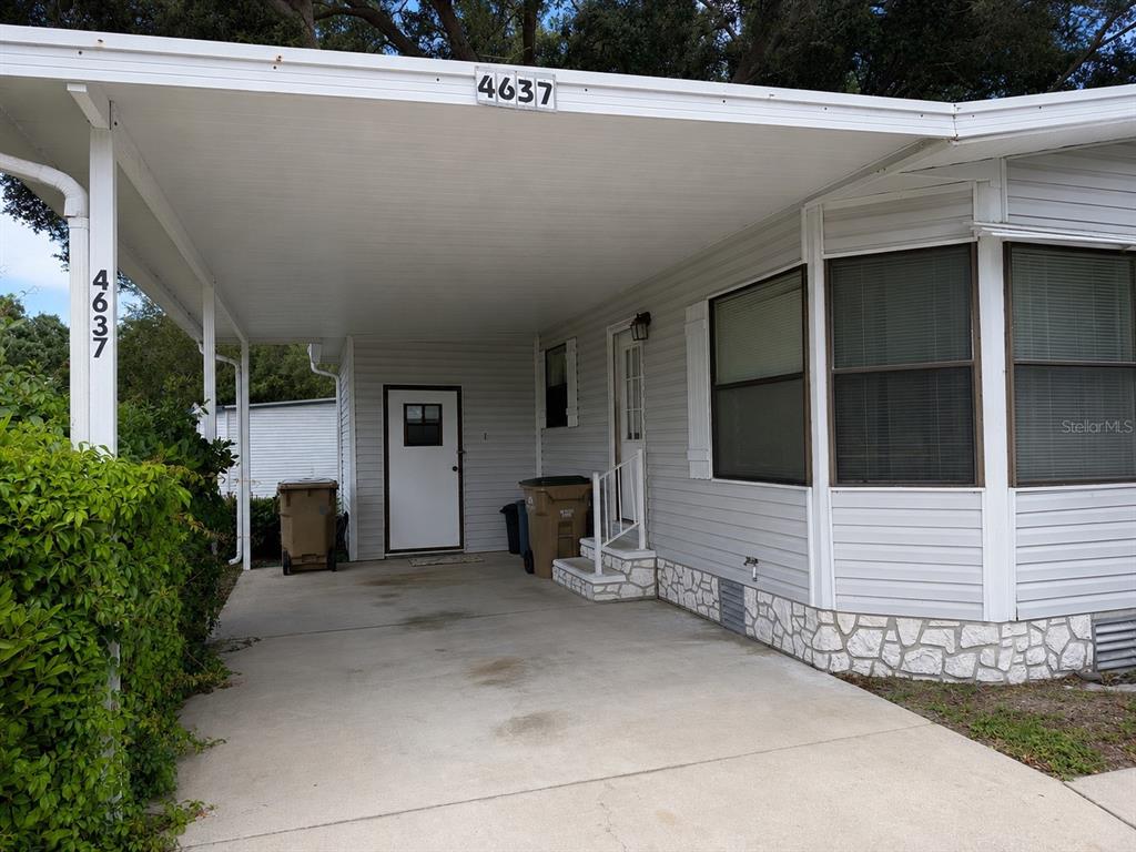 A white mobile home exterior features a covered carport, concrete driveway, and stone-patterned skirting — 4637 BELLE GROVE, LEESBURG, FL