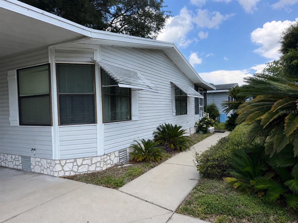 A light-colored mobile home exterior features horizontal siding, stone-patterned skirting, and metal window awnings — 4637 BELLE GROVE, LEESBURG, FL