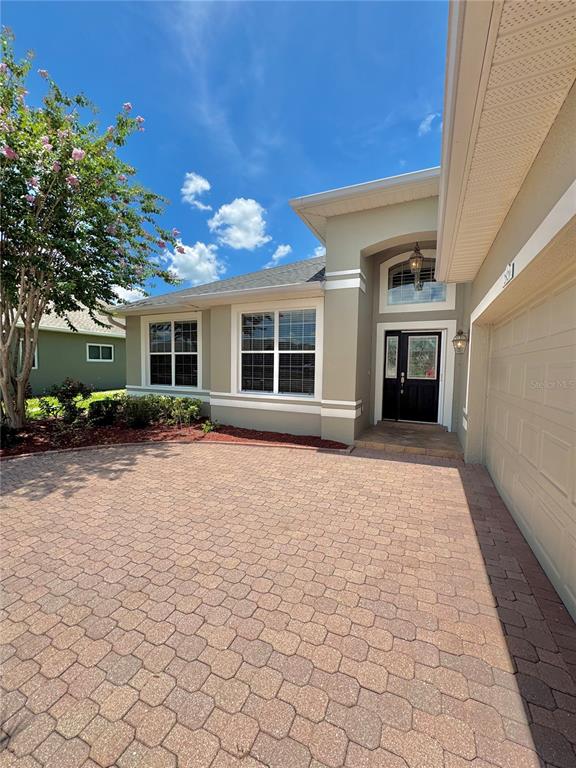 A beige house exterior features a paved driveway, a dark front door, and a garage — 2820 TRADITIONS BOULEVARD S, WINTER HAVEN, FL